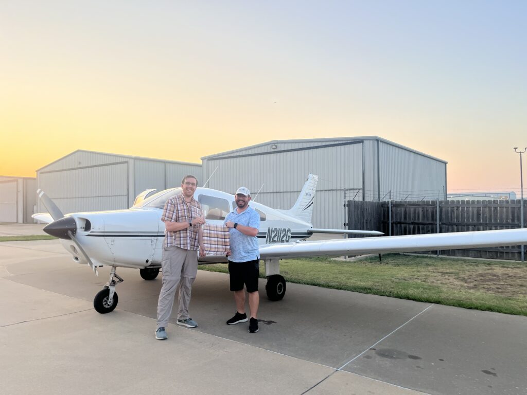 Josh and instructor Nathan holding removed shirt tail in front of airplane.